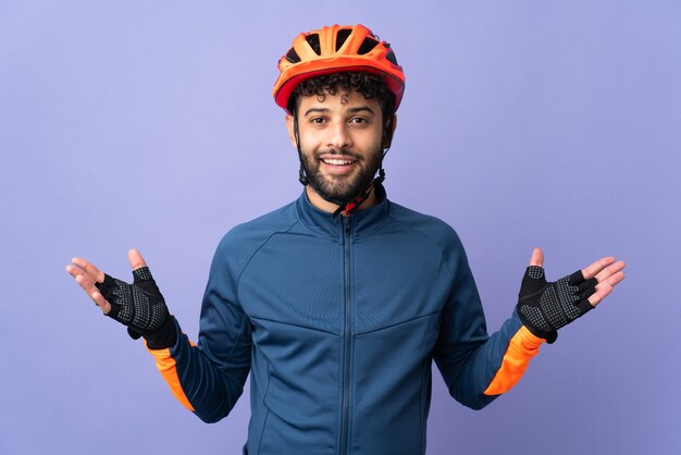 Uomo giovane ciclista marocchino isolato sulla parete viola con espressione facciale scioccata