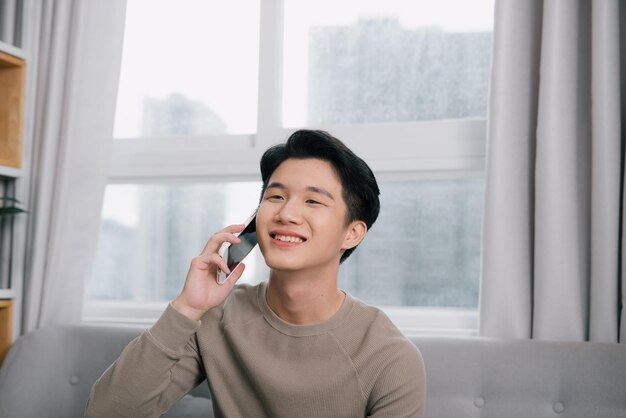 Uomo giovane e sano, sorridente e parlando al telefono intelligente a casa