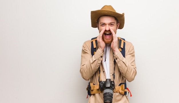 Uomo giovane esploratore di redhead che grida qualcosa di felice alla parte anteriore. In possesso di una macchina fotografica.