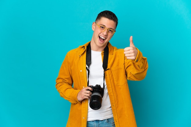 Uomo giovane fotografo caucasico isolato sulla parete blu con i pollici in su perché è successo qualcosa di buono