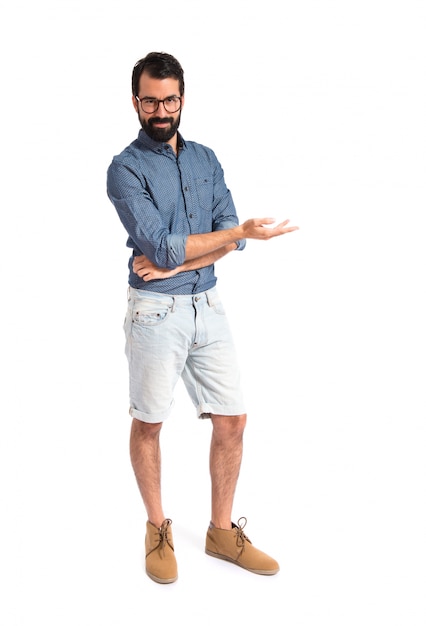 Uomo giovane hipster che presenta qualcosa su sfondo bianco