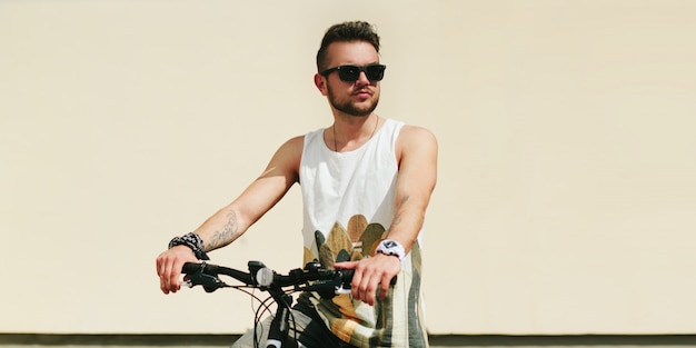 Uomo giovane hipster con bici in città in una giornata di sole estivo