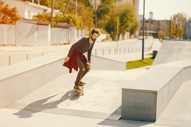 uomo giovane hipster in piedi in un parco soleggiato estate con uno skateboard nelle sue mani