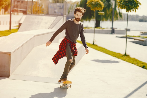 uomo giovane hipster in piedi in un parco soleggiato estate con uno skateboard nelle sue mani