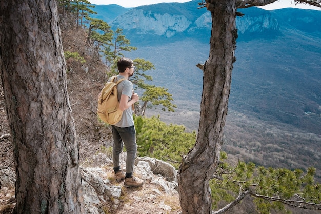 Uomo giovane hipster nelle montagne primaverili. Hipster con uno zaino dietro la schiena va in viaggio