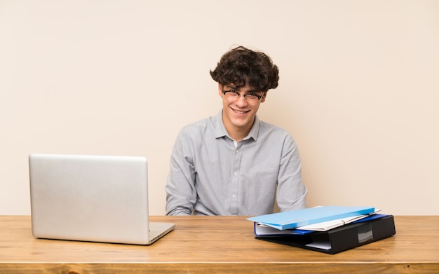 Uomo giovane studente con un computer portatile con gli occhiali e felice