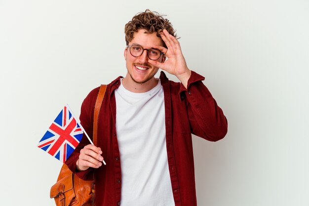 Uomo giovane studente imparare l'inglese isolato sul muro bianco eccitato mantenendo il gesto giusto sull'occhio.