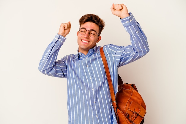 Uomo giovane studente isolato sul muro bianco che celebra un giorno speciale, salta e alza le braccia con energia.