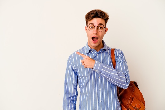 Uomo giovane studente isolato sul muro bianco che punta di lato