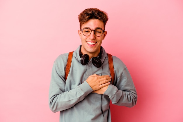 Uomo giovane studente isolato sulla parete rosa che ride mantenendo le mani sul cuore, il concetto di felicità.