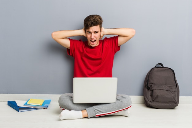 Uomo giovane studente seduto sul suo pavimento di casa in possesso di un computer portatile