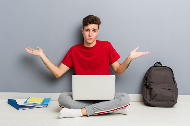 Uomo giovane studente seduto sul suo pavimento di casa in possesso di un computer portatile