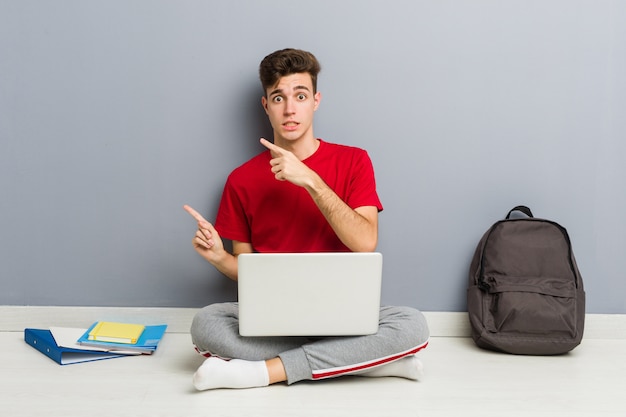 Uomo giovane studente seduto sul suo pavimento di casa in possesso di un computer portatile