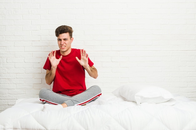 Uomo giovane studente studente sul letto rifiutando qualcuno che mostra un gesto di disgusto.