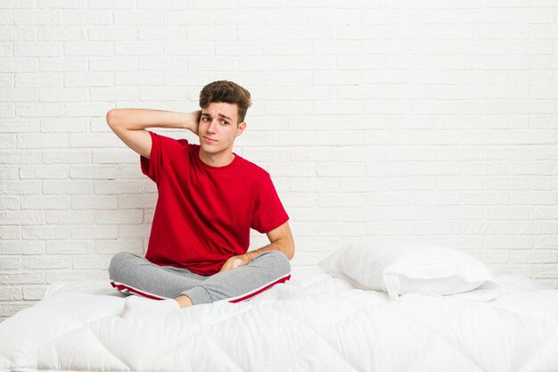 Uomo giovane studente studente sul letto toccando la parte posteriore della testa, pensando e fare una scelta.