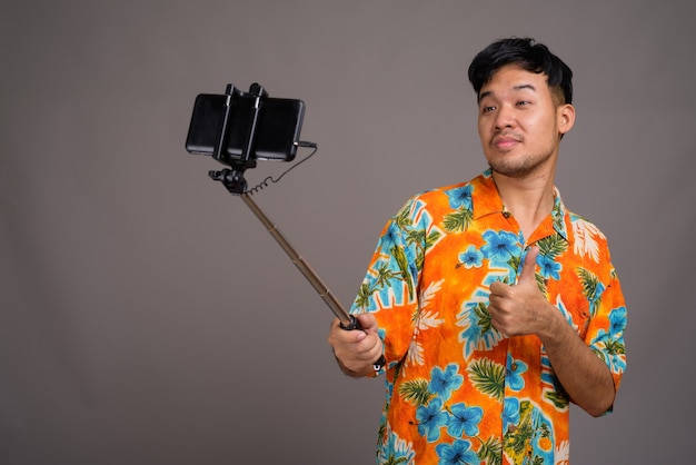 Uomo giovane turista asiatico pronto per le vacanze contro il grigio