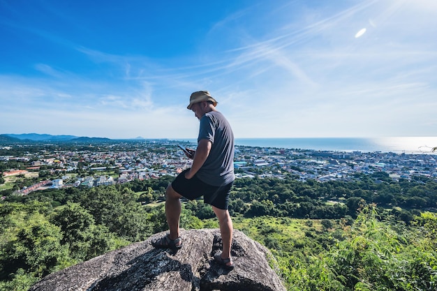 Uomo grasso asiatico in piedi sulla roccia guarda il telefono al punto di vista di Khao hin lek faiKhao Hin Lek Fai è un posto per vedere una vista spettacolare dell'intera cittàConosciuto anche come radar khao nella popolazione locale