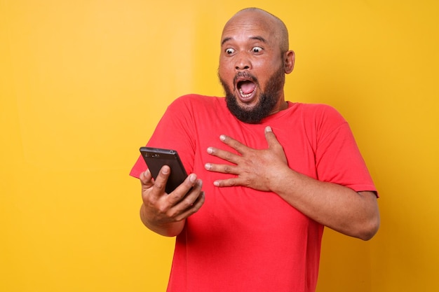 Uomo grasso barbuto in camicia rossa che si sente scioccato e sorpreso quando guarda lo smartphone