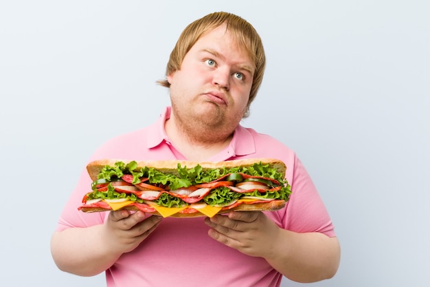 Uomo grasso biondo pazzo caucasico che tiene un panino gigante