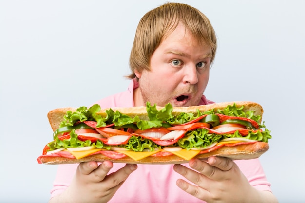 Uomo grasso biondo pazzo caucasico che tiene un panino gigante