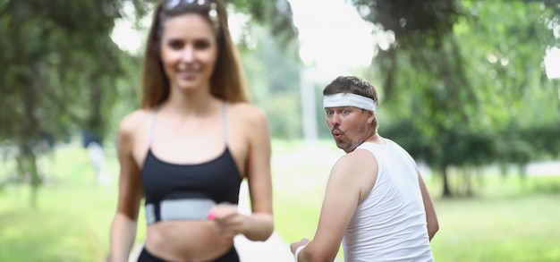 Uomo grasso che guarda una giovane atleta che fa jogging nel parco