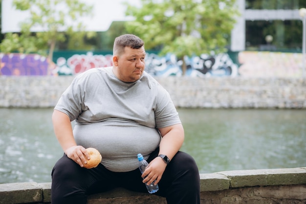 Uomo grasso che mangia un hamburger e acqua durante l'allenamento allo stadio