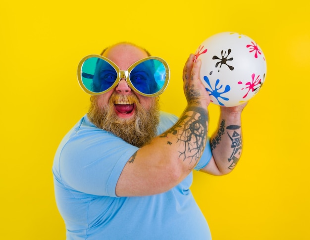 Uomo grasso con barba e occhiali da sole si diverte con una palla