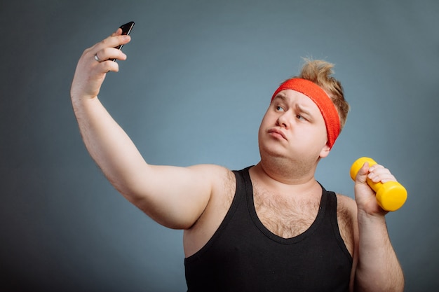 Uomo grasso con la grande pancia, tenendo il manubrio, facendo selfie sulla parete grigia