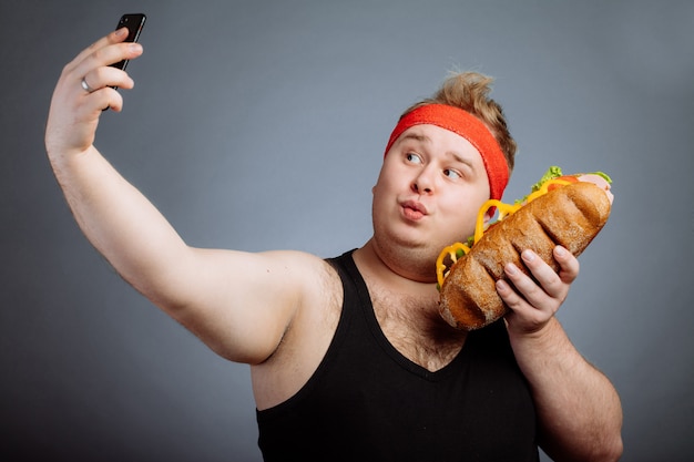 Uomo grasso con sandwich in mano rende selfie