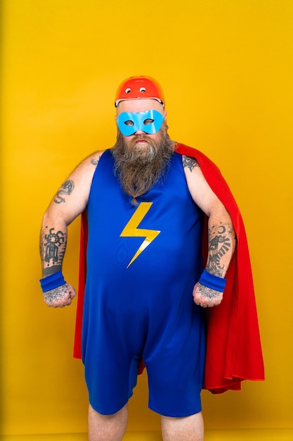 Uomo grasso divertente con costume da supereroe che funge da sovrumano con poteri speciali ritratto sulla parete colorata