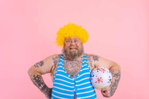 Uomo grasso e felice con barba e parrucca gioca con la palla