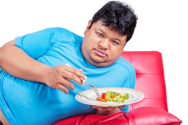 Uomo grasso infelice che mangia cibo sano in studio