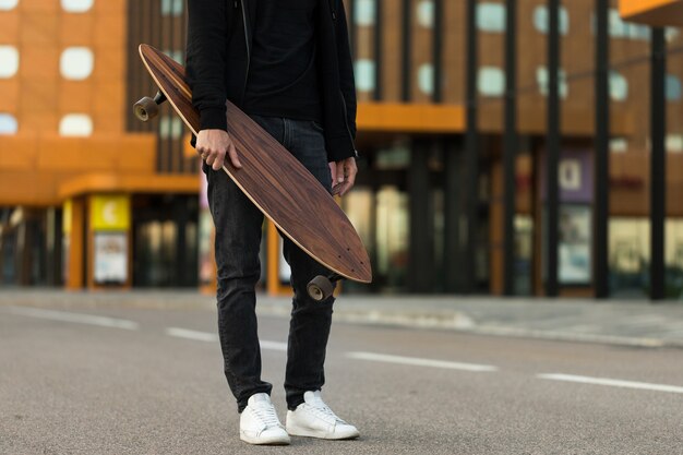 Uomo hipster che tiene skateboard o tavola lunga all'aperto