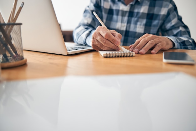Uomo impegnato a prendere appunti durante la riunione online mentre lavora dal suo ufficio a casa