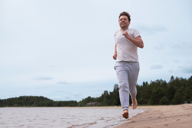 Uomo in abbigliamento fitness che corre lungo la spiaggia sabbiosa