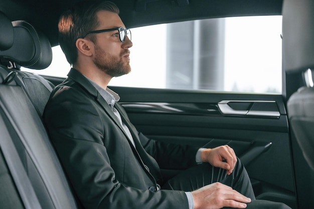 Uomo in abiti da lavoro formali è seduto nell'automobile moderna
