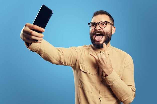 Uomo in abito alla moda che urla e mostra un gesto rock mentre fa selfie