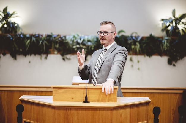 Uomo in abito grigio che predica le parole della Sacra Bibbia all'altare di una chiesa