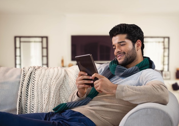 Uomo in autunno con tablet e sciarpa sul divano di casa