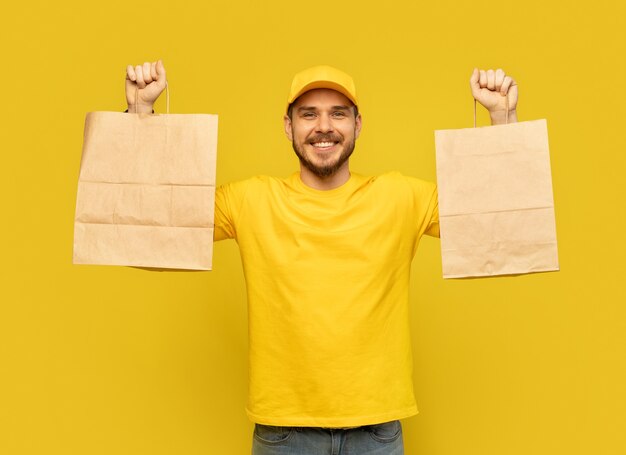 Uomo in berretto giallo, maglietta che dà i pacchetti di carta isolati. Corriere dipendente maschio tenere pacchetti di carta con il cibo