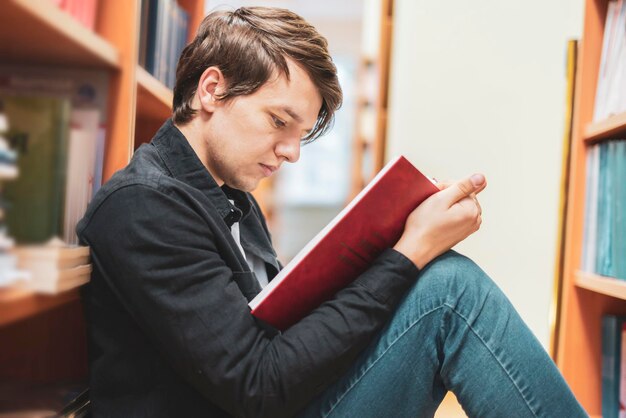 uomo in biblioteca che legge un libro seduto sotto lo scaffale b