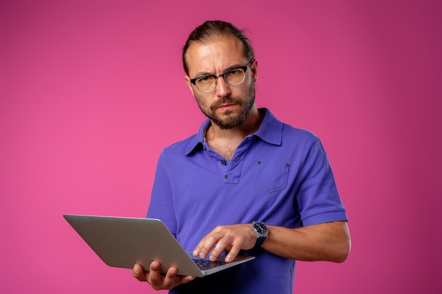 Uomo in bicchieri in piedi con il computer portatile su sfondo rosa