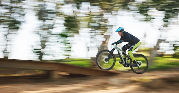 Uomo in bicicletta e velocità con sfocatura di movimento nella foresta per gare sportive o avventure nei boschi estivi o nella natura Persona in bicicletta estremamente veloce e azione su allenamento in pista o sfida per il fitness in bicicletta