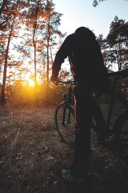 Uomo in bicicletta nella foresta autunnale la sera al tramonto