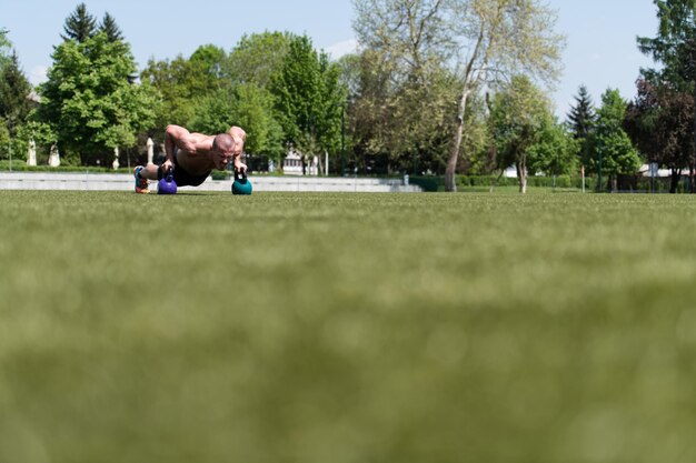 Uomo in buona salute che fa flessioni sull'erba con Kettlebell