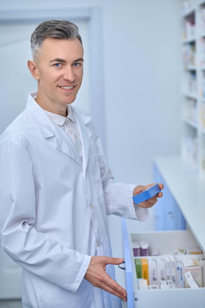 Uomo in camice da laboratorio in piedi vicino agli scaffali con medicine