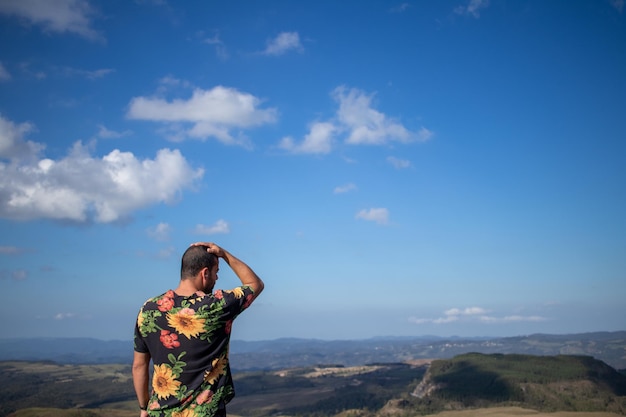 uomo in camicetta a fiori che ammira il paesaggio con la mano sulla testa con le spalle alla foto