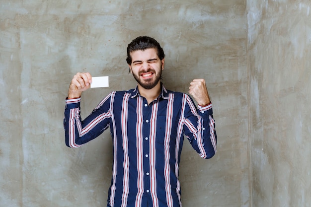 Uomo in camicia a righe che tiene il suo biglietto da visita e si gode la sua nuova posizione