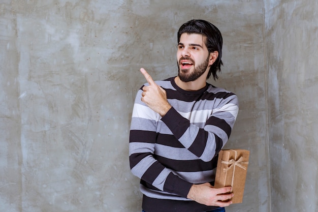 Uomo in camicia a righe che tiene una scatola regalo di cartone e indica da qualche parte