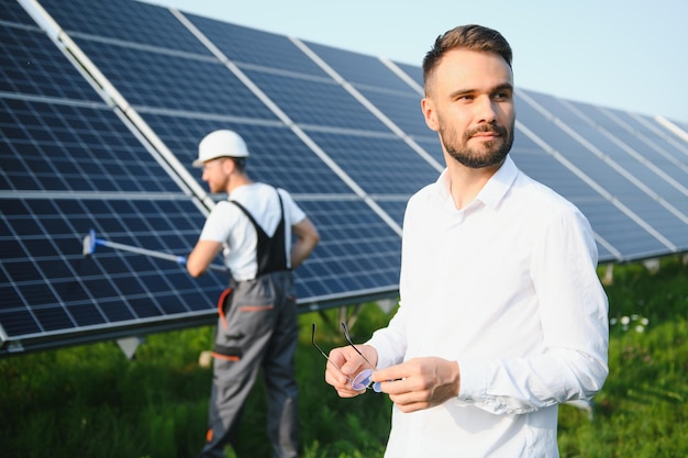 Uomo in camicia bianca in piedi vicino a pannelli fotovoltaici in giornata di sole in campagna